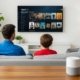 A father and son sitting on a sofa watching movies on a wall mounted smart TV in a modern living room with indoor plants and stylish decor.